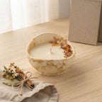 Vela Hora dorada en cuenco ovalado marmolado ocre, decorada con flores secas, virutas de madera y un detalle color ámbar